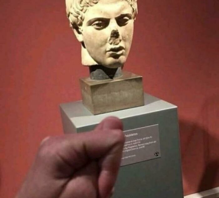 A hand points towards a damaged stone bust on a red background, showcasing unhinged images.