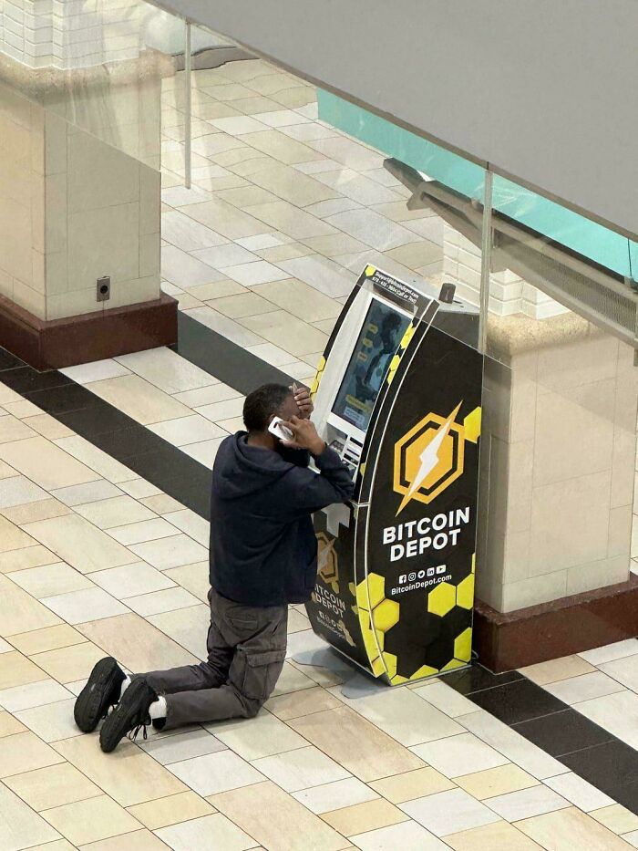A man kneeling and talking on his phone in front of a Bitcoin Depot ATM, an unhinged image.