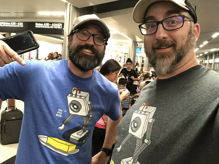 Two men in an airport, both wearing shirts with the same robot design, an amazing example of something synced just right.