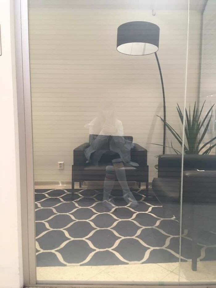 A person sitting in a chair, reflected perfectly in a glass door, creating an illusion of being synced just right.