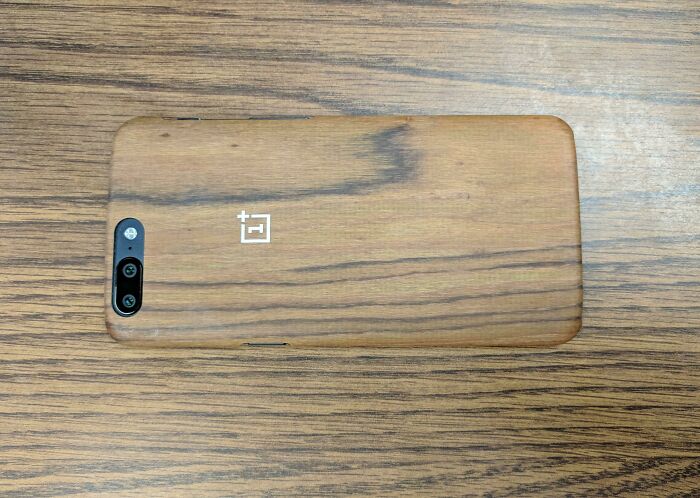 A OnePlus phone with a wood grain case, perfectly synced to the wooden table pattern below.