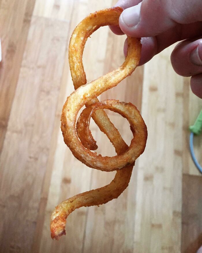 A curly fry held up, amazingly synced into the shape of a musical treble clef.