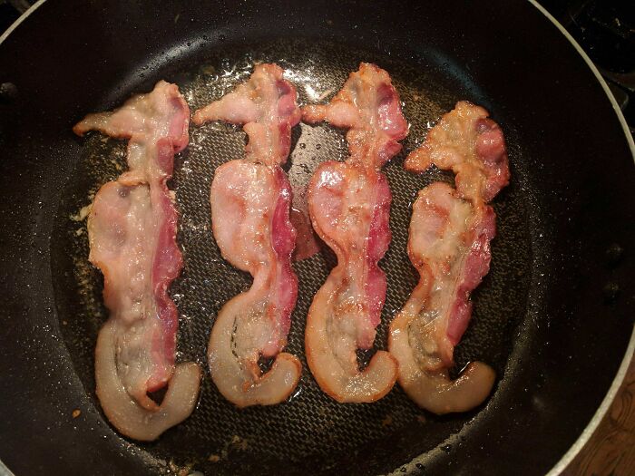 Bacon strips frying in a pan, perfectly synced to form seahorses, an amazing sync just right.