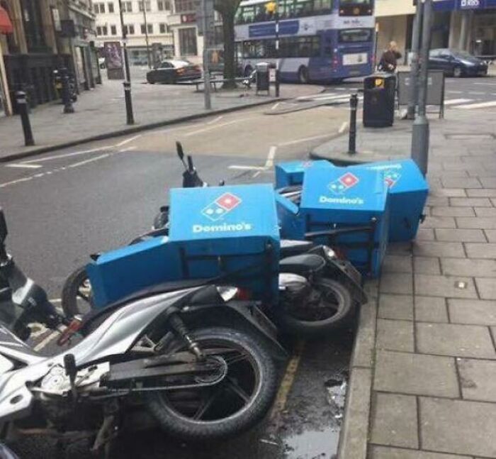 Several Domino's delivery motorcycles synced on their sides along a city curb after something happened.