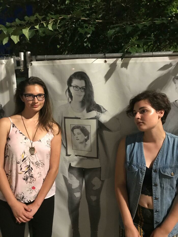 Two young women standing in front of a poster of a woman, with one girl's face perfectly synced with the framed photo on the poster.