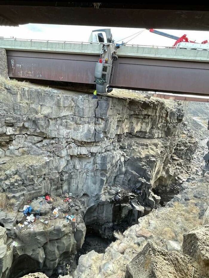 A semi-truck hanging precariously off a bridge over a deep canyon, showcasing an amazing synced moment of peril.