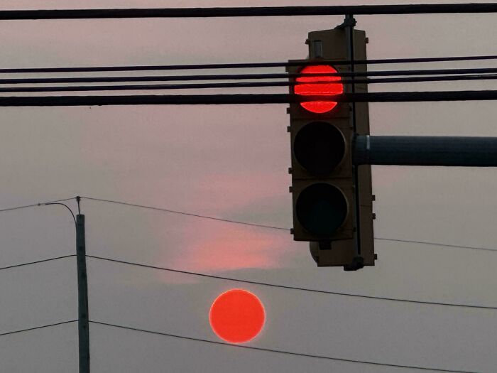 A traffic light with a red stop signal, perfectly synced with the red setting sun below it.