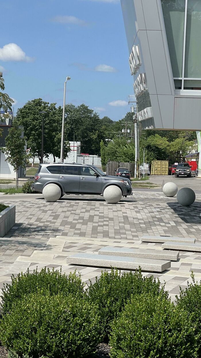 A grey SUV parked, its wheels perfectly aligned with two large spherical bollards, an amazing something Synced Just Right.