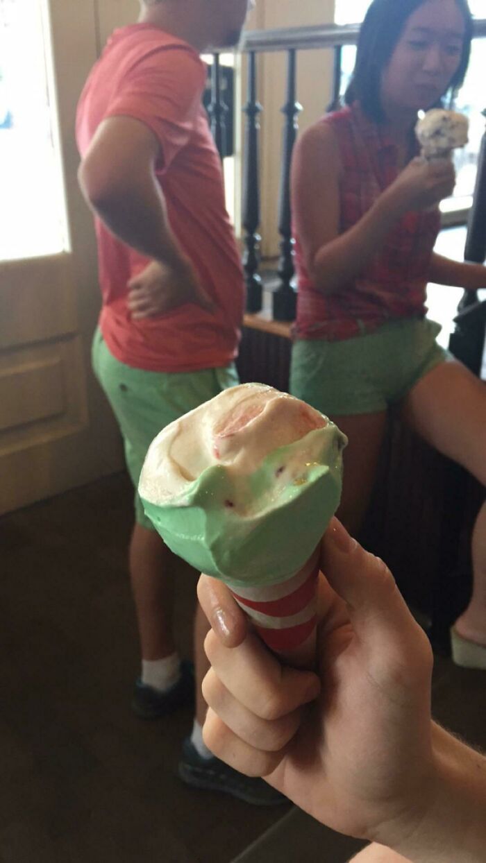 A person holding an ice cream cone in front of two people, all wearing clothes that synced just right.