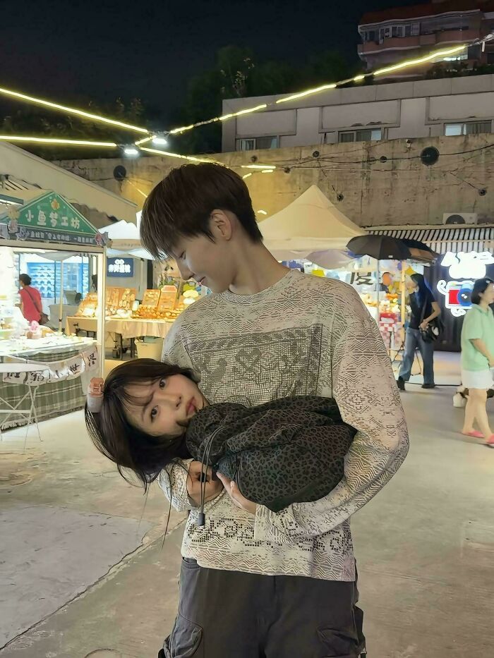 A man holding a woman upside down at a night market, an unhinged image of playful interaction.