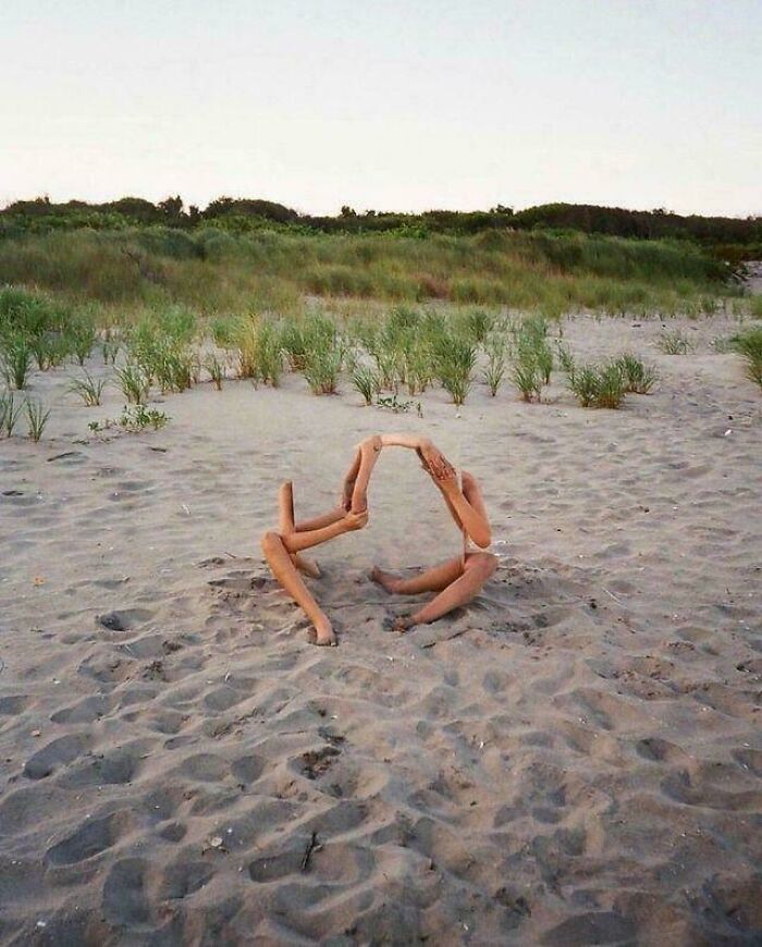 Two people intertwined on a sandy beach, their limbs creating an unhinged and abstract image.