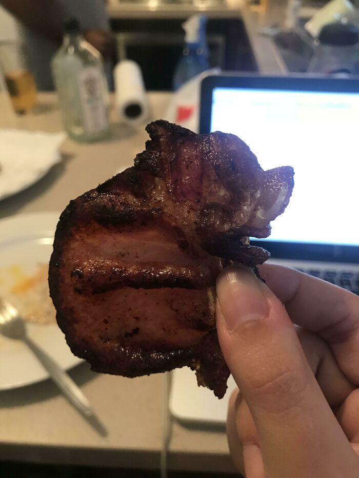 A piece of grilled meat, remarkably synced with the shape of a pig's head, held by fingers.