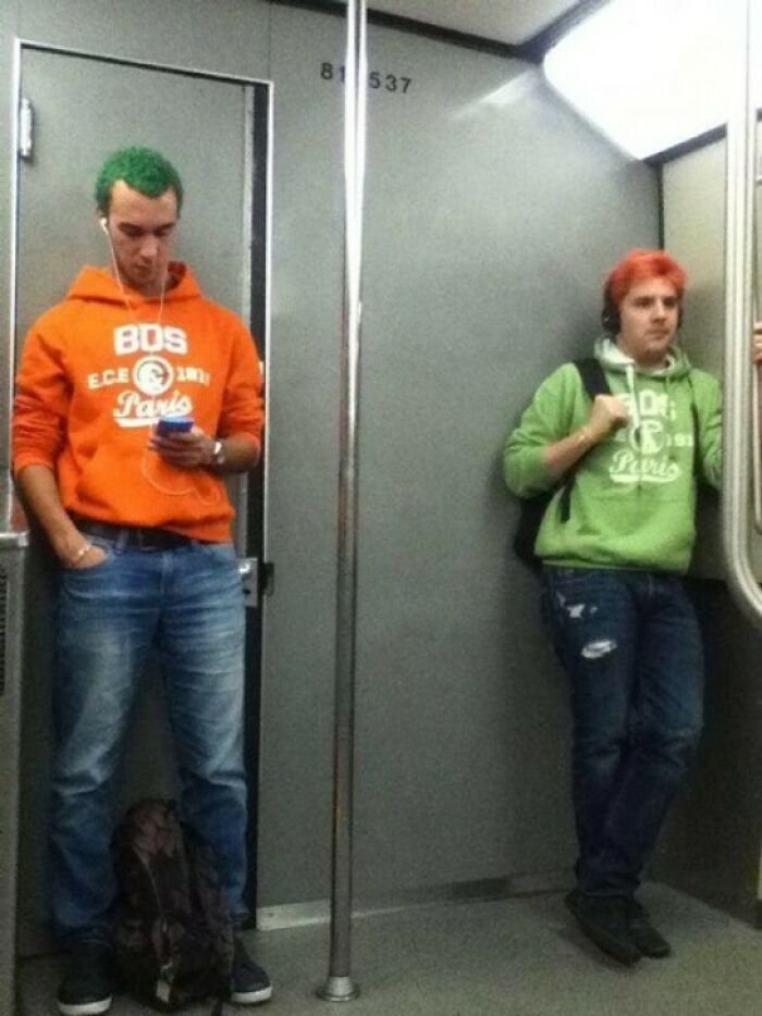 Two men on a subway, wearing swapped colored outfits and hair, amazing times something synced just right.