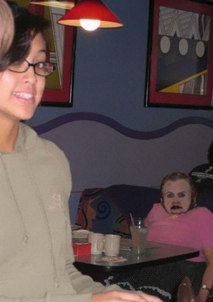 A young woman smiles while an unhinged image of a person with an unusual face sits in the background.