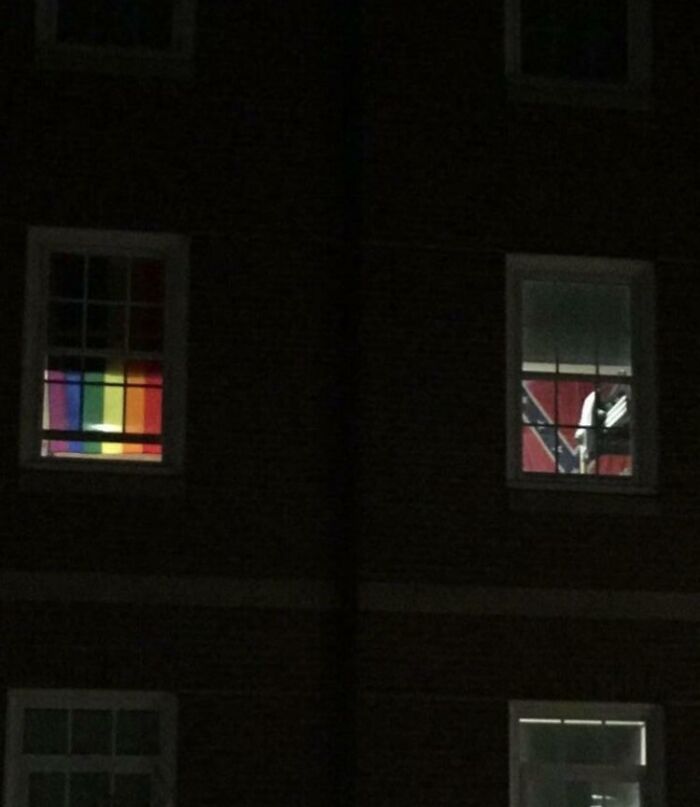 Two unhinged images through windows; one with a pride flag, the other with a Confederate flag.