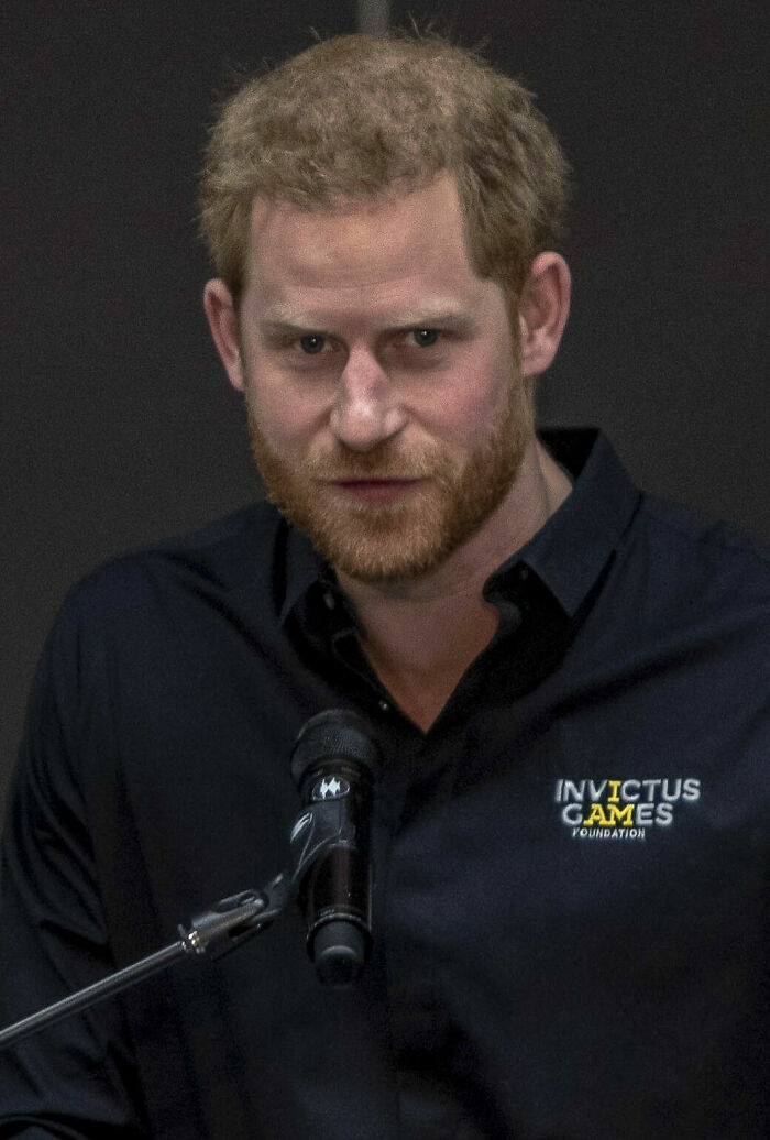 Prince Harry speaking at a microphone, wearing a black shirt with the Invictus Games Foundation logo, showcasing his career highlights.