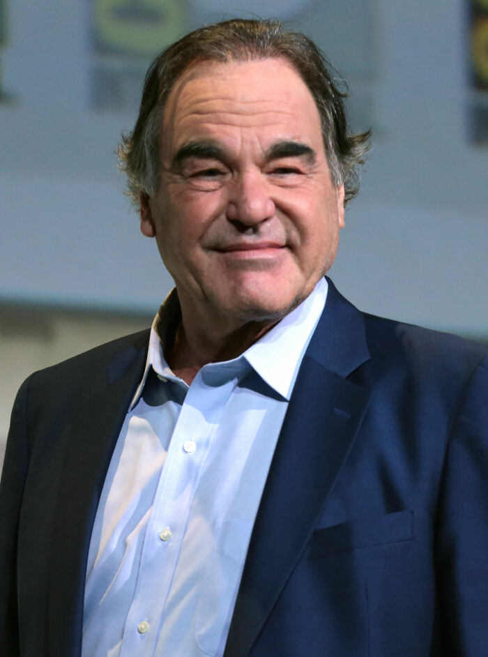 A close-up of Oliver Stone smiling, featuring his bio and career highlights.