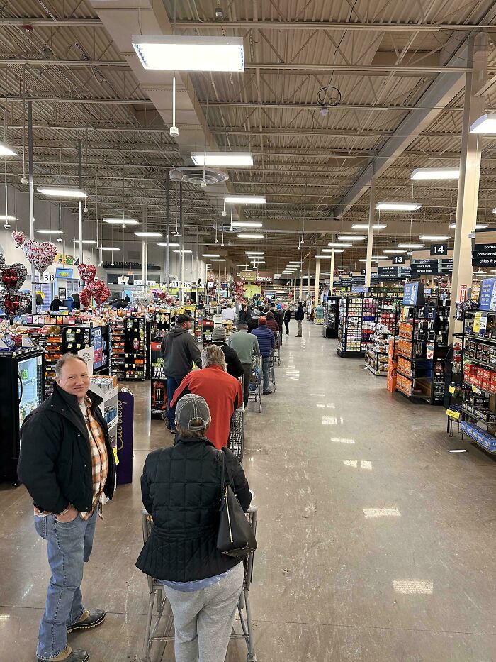 A long line of people in a grocery store, illustrating products and services getting worse while expensive.