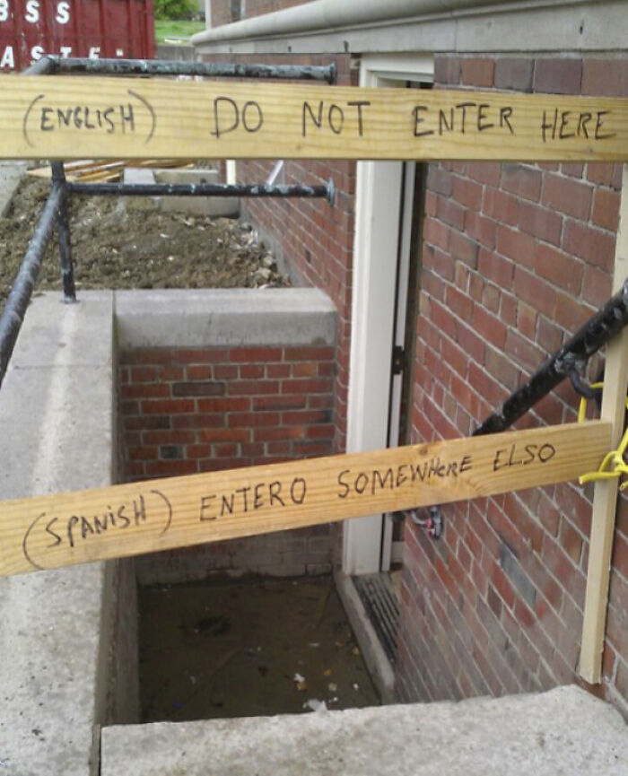 A chaotic sign in the wild: wooden planks reading ENGLISH DO NOT ENTER HERE and SPANISH ENTERO SOMEWHERE ALSO.