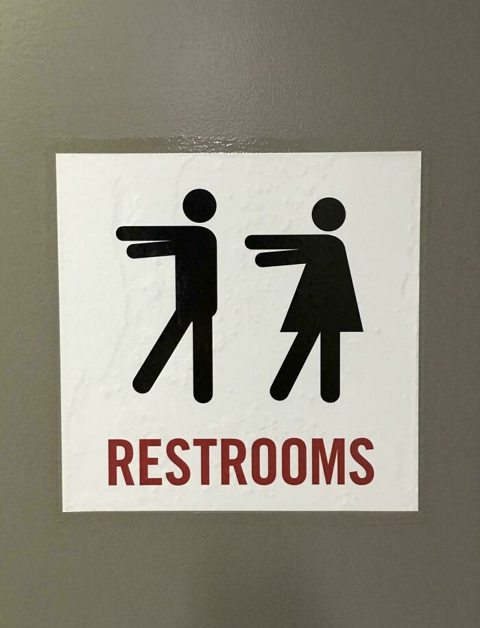 A chaotic sign for restrooms with male and female figures seemingly pushing each other, spotted in the wild.