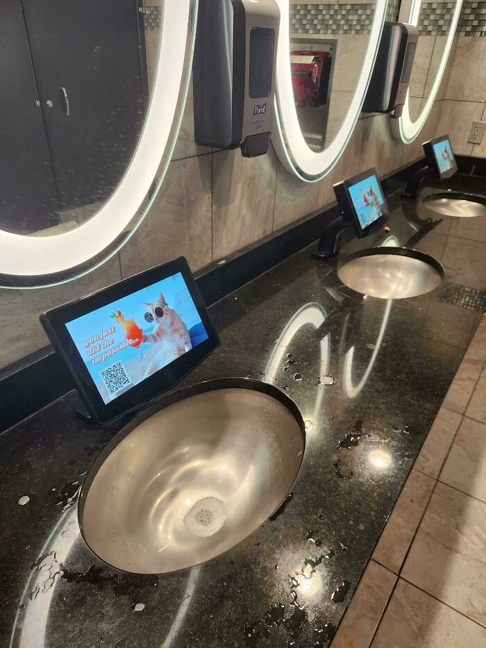 A public restroom with dirty sinks and screens displaying an ad, symbolizing products and services getting worse while more expensive.