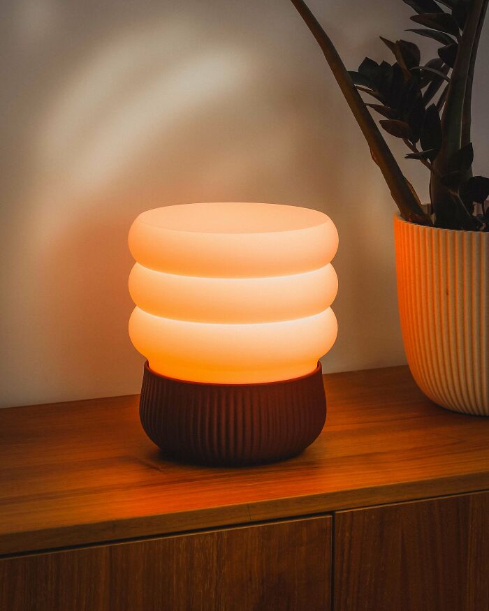A modern, glowing lantern 3D printed with a ribbed base, casting a warm light on a wooden surface.
