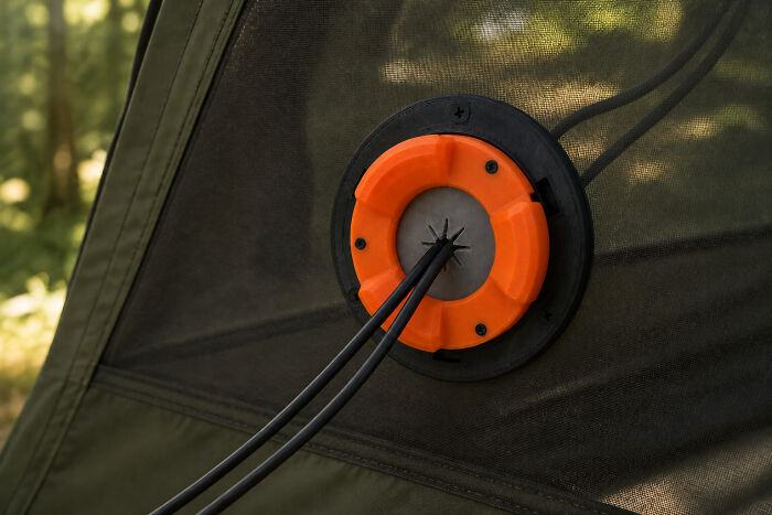 A practical orange 3D printed cable pass-through attachment on a tent, securing cords neatly.