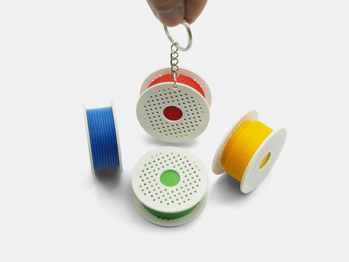 Collection of miniature 3D printed filament spools in red, blue, green, and yellow, one used as a keychain.