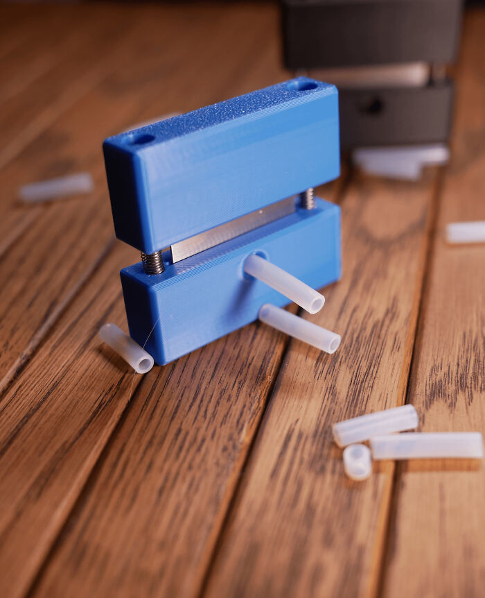 A blue 3D printed tool on a wooden surface, with several small white tubes inserted, demonstrating its function.