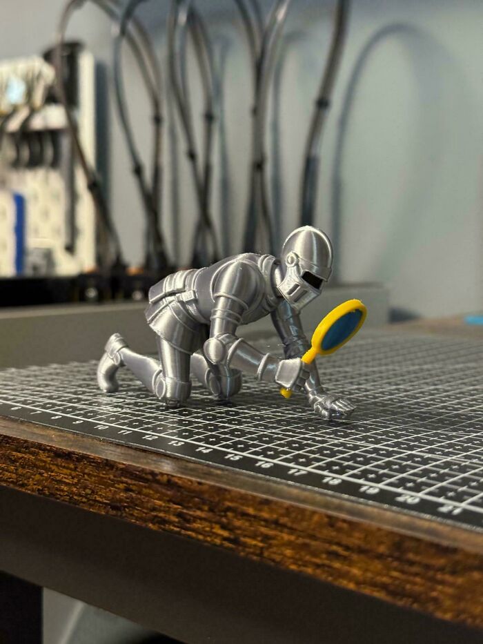 A small, detailed 3D printed knight in shining armor, kneeling and holding a tiny magnifying glass.
