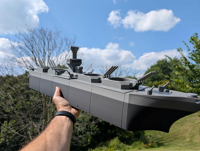 A person holding a large, detailed model battleship against a blue sky, showcasing items people 3D printed.
