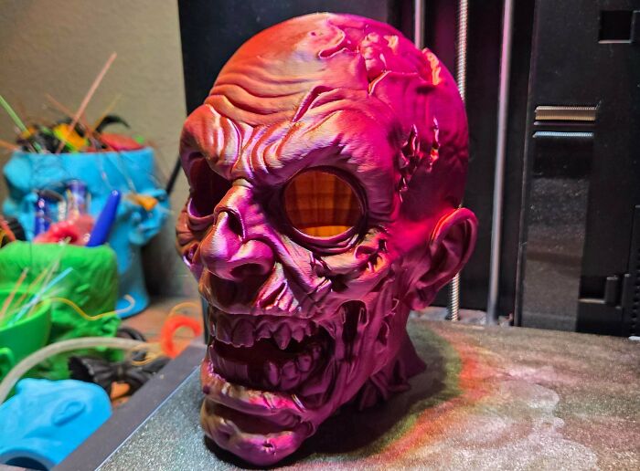 A detailed, multicolored 3D printed zombie skull with glowing eyes, demonstrating something people needed and 3D printed.