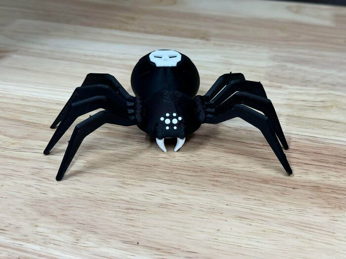 A black 3D printed spider with white markings and fangs, a creation made by people using 3D printers.
