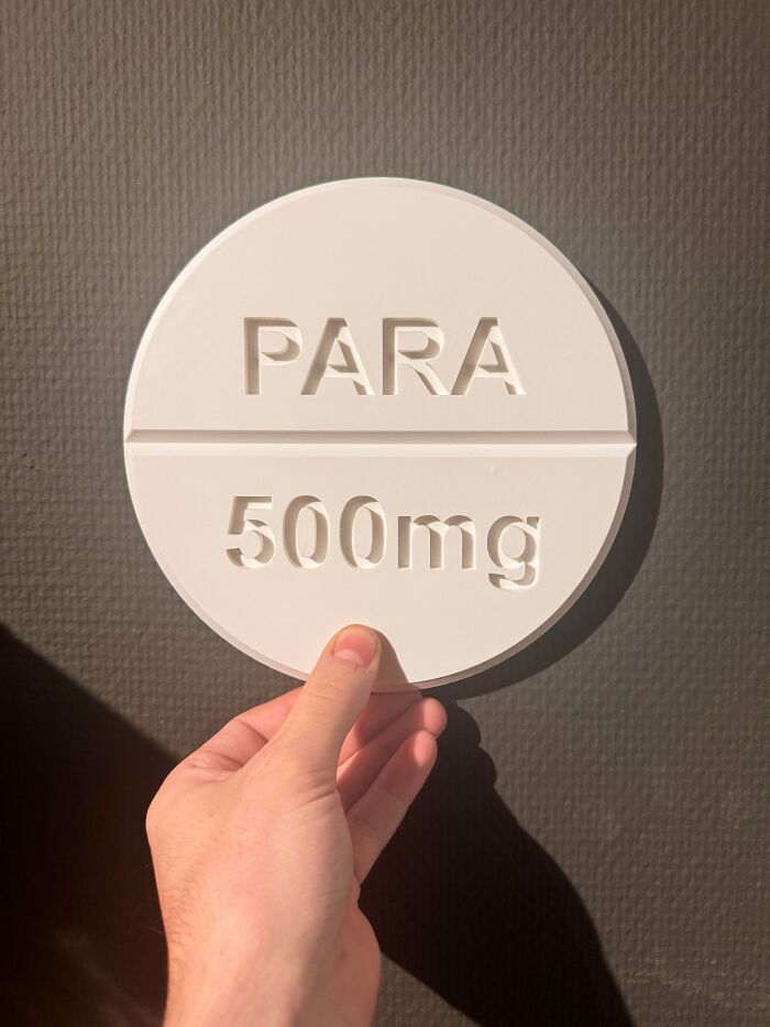 A hand holding a large, round 3D printed model of a white medicine pill labeled PARA 500mg.