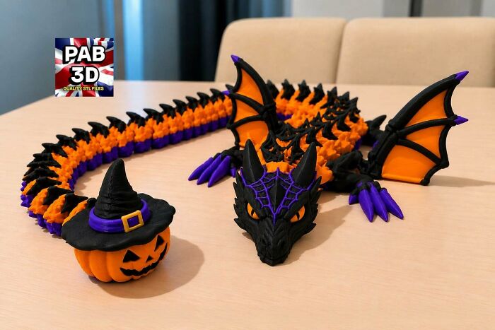 A 3D printed Halloween dragon in black, orange, and purple, next to a pumpkin wearing a witch hat, showing off unique 3D printers.