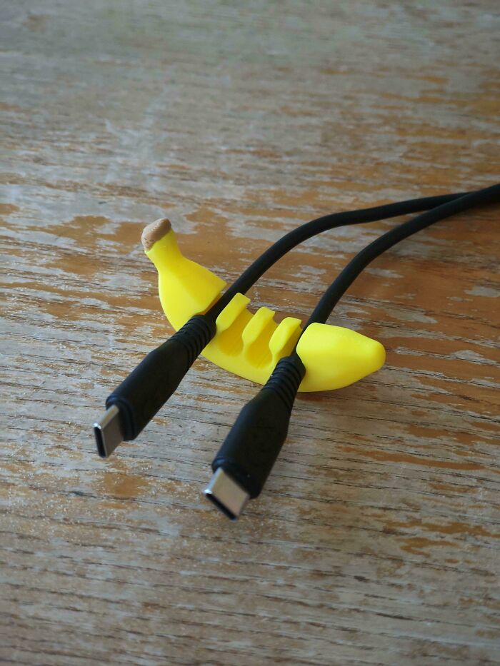 A banana-shaped cable organizer holding two black cables, an item produced by 3D printers.