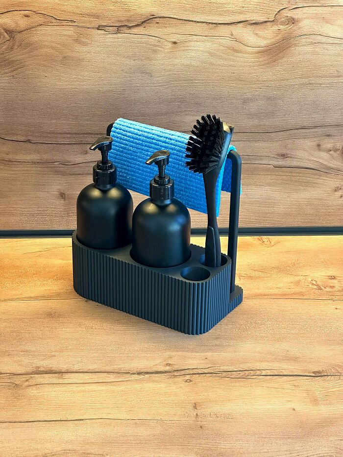 A black kitchen organizer for dish soap, a brush, and a cloth, demonstrating functional items from 3D printers.