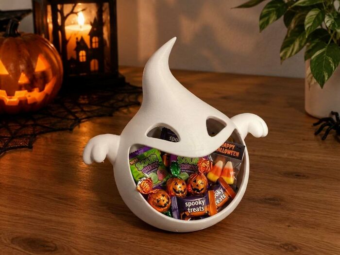 A white ghost-shaped candy bowl, filled with Halloween treats, exemplifies custom objects made by 3D printers.