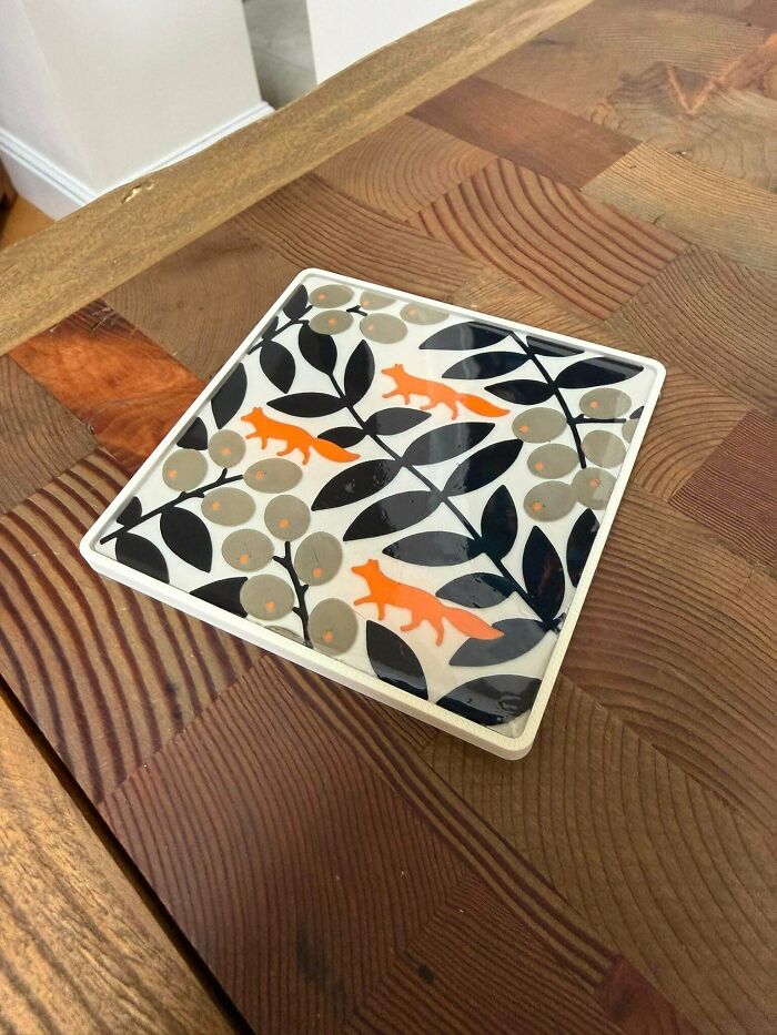 A square coaster with orange foxes and black and gray leaves, a practical item created with 3D printers.