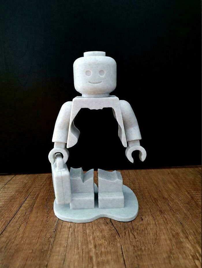 A unique 3D printed LEGO figure, half-dissolved, holding a briefcase on a wooden surface, showcasing creative 3D printers.