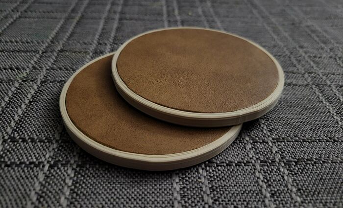 Two elegant circular coasters with a leather-like top, precisely 3D printed to protect surfaces.