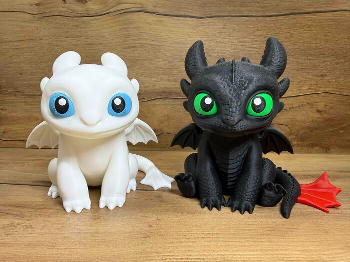 Two cute 3D printed dragon figures, one white and one black, with colorful eyes, showing fun uses for 3D printers.