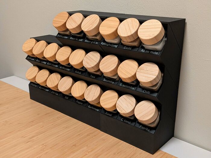 A tiered black 3D printed spice rack holding multiple spice jars with wooden lids, an organized solution from 3D printers.