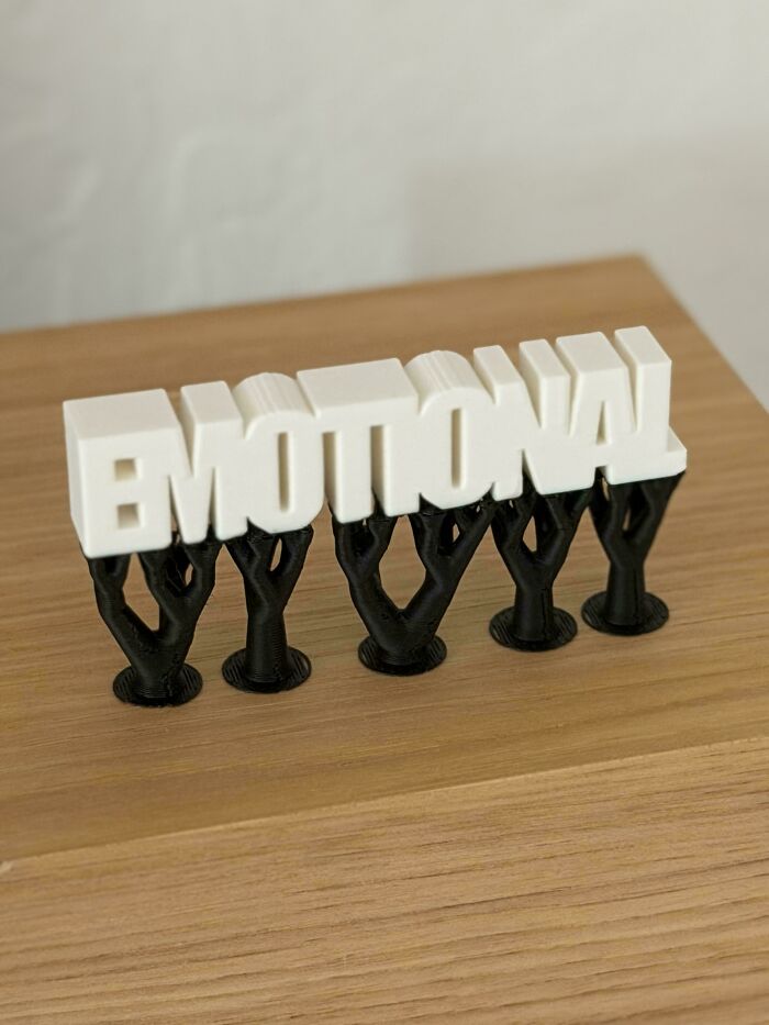 A 3D printed model of the word EMOTIONAL in white with black supports, showcasing creativity with 3D printers.
