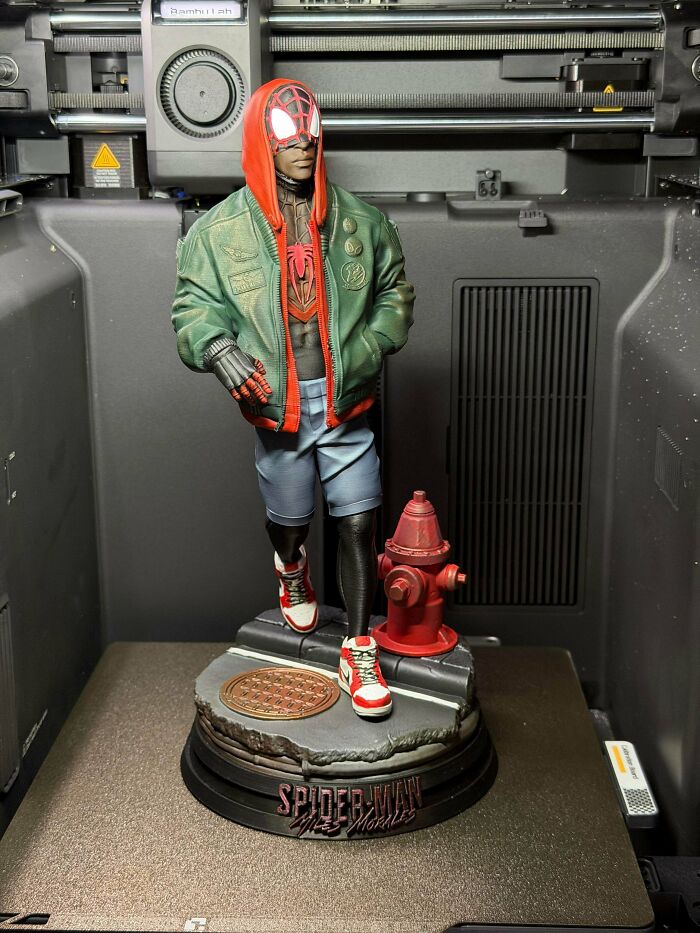 A detailed 3D printed Miles Morales Spider-Man statue with a fire hydrant, showcased on a printer bed.