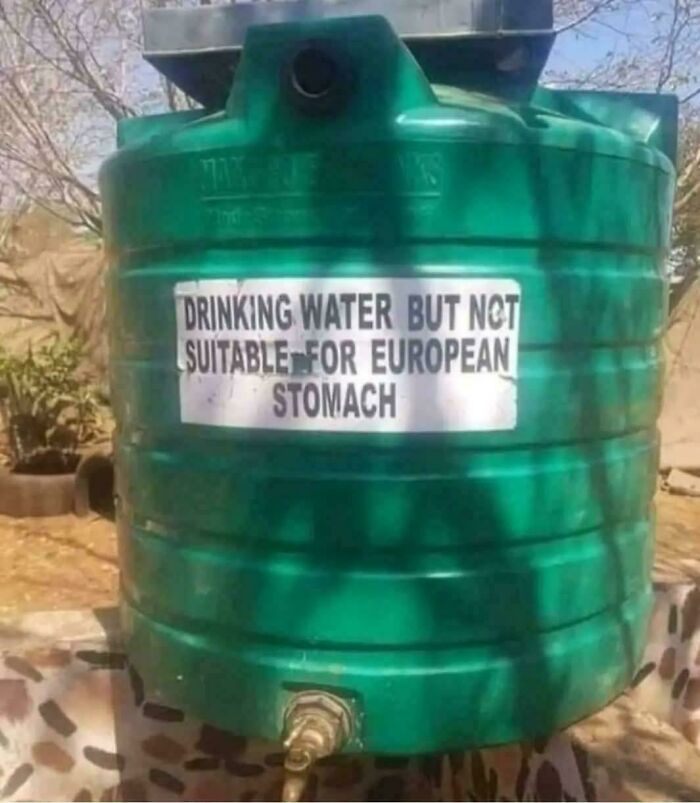 A water tank with a chaotic sign in the wild: Drinking water but not suitable for European stomach.