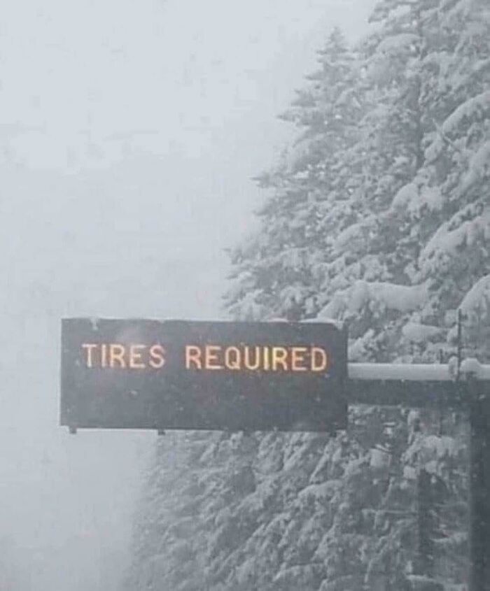 A chaotic sign in the wild showing TIRES REQUIRED on an electronic board during a snowstorm.