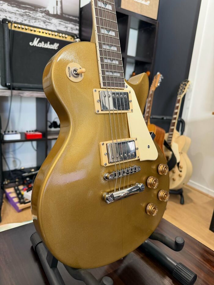 A shiny gold electric guitar on a stand, a musical instrument people needed and printed with their 3D printers.