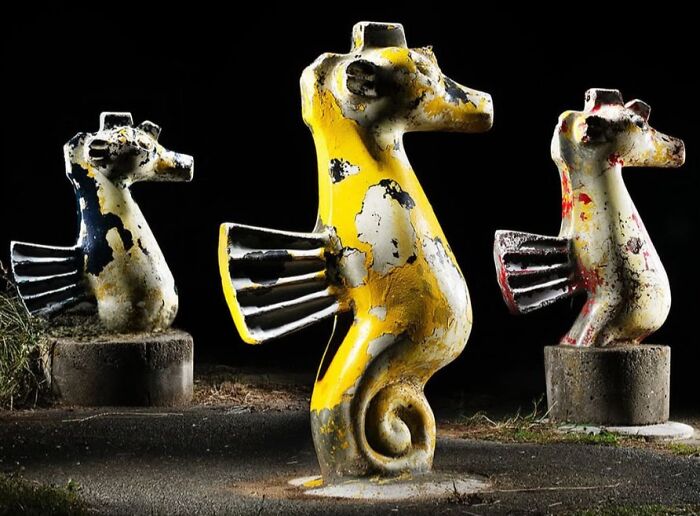 Three weathered seahorse-shaped sculptures, one vibrant yellow, in a Japanese playground at night by Fujio Kito.