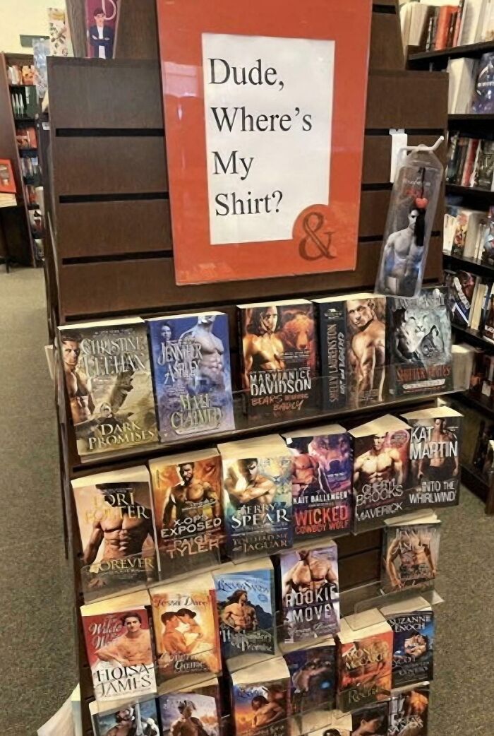 A chaotic sign spotted in the wild, a book display with a sign reading Dude, Where's My Shirt? above romance novels.